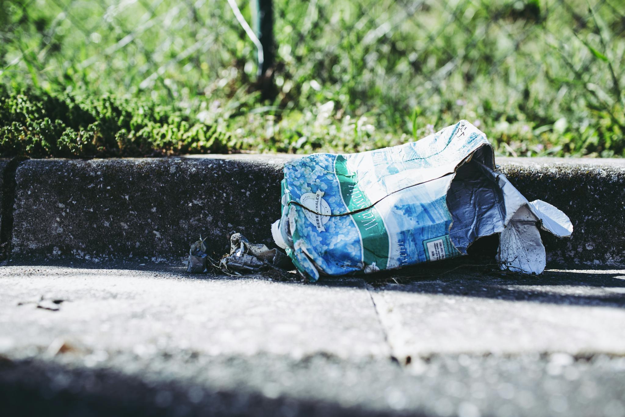 A crumpled bag lies on a sidewalk next to a fence, highlighting urban waste issues.