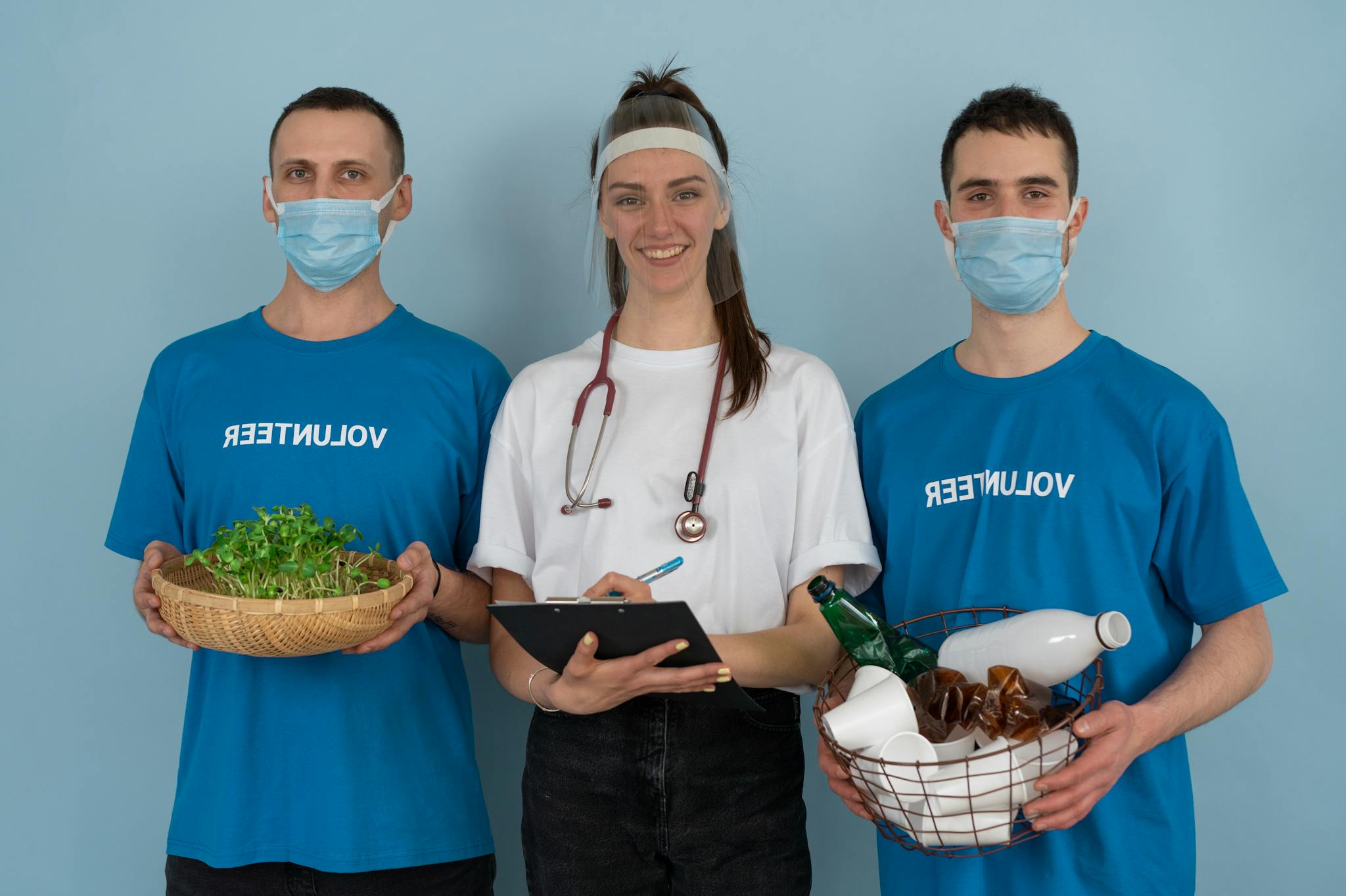 Three volunteers promoting eco-friendly practices with plants and recycling materials.
