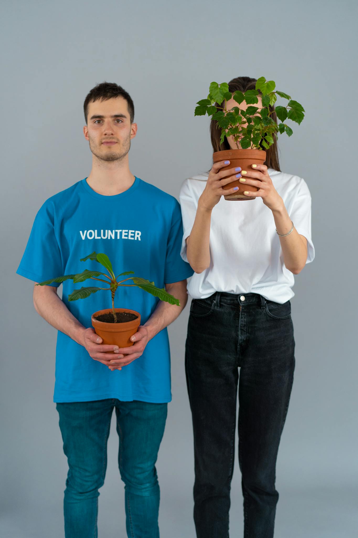 Two people holding potted plants symbolizing eco-friendly volunteer work.