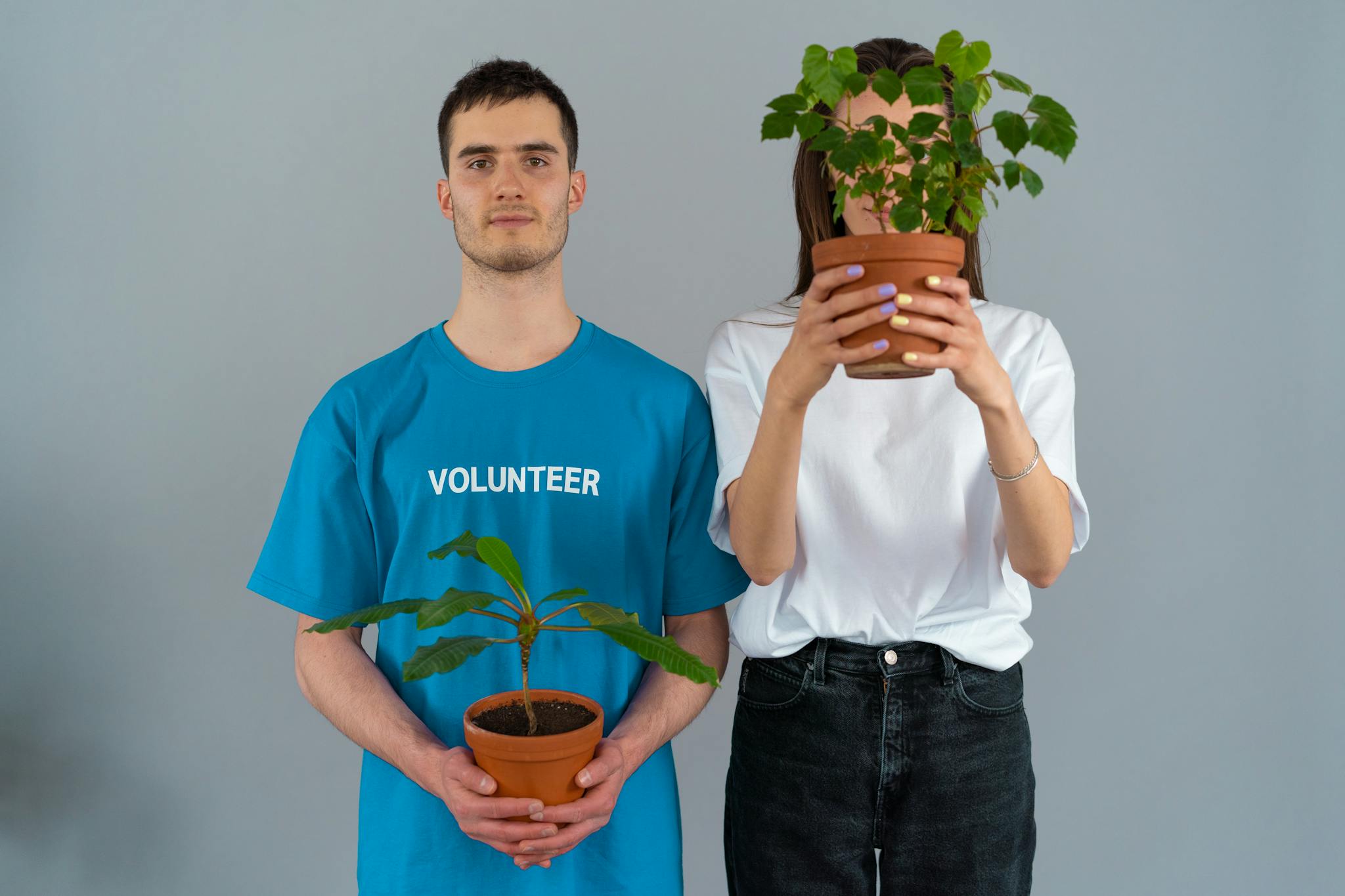 Two volunteers holding potted plants, symbolizing green conservation and volunteering efforts.