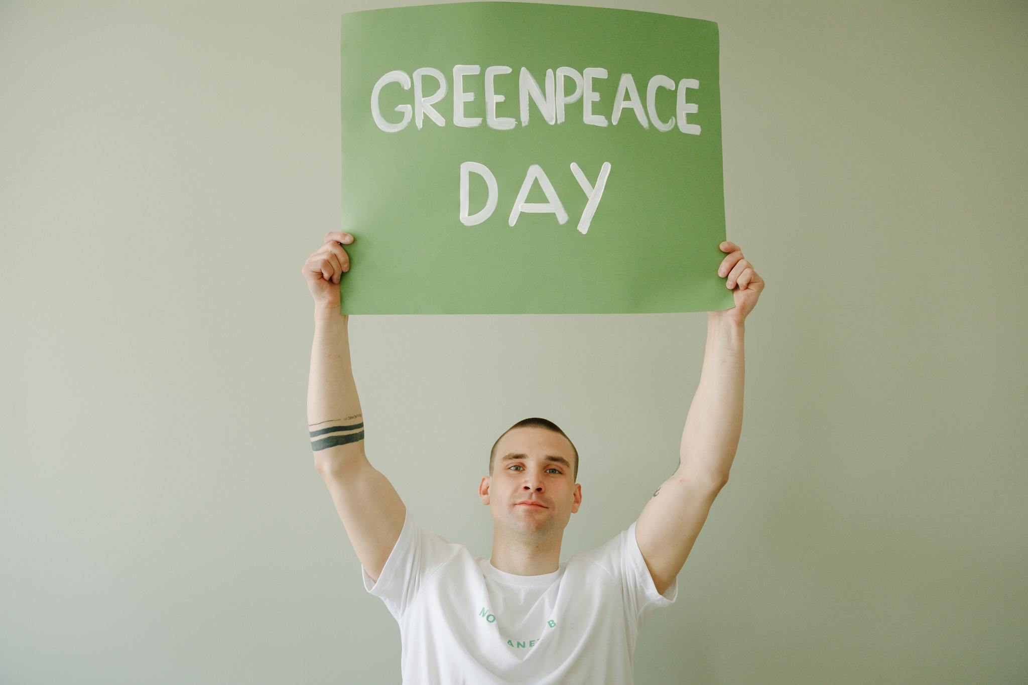 Young man promoting Greenpeace Day with green banner indoors.